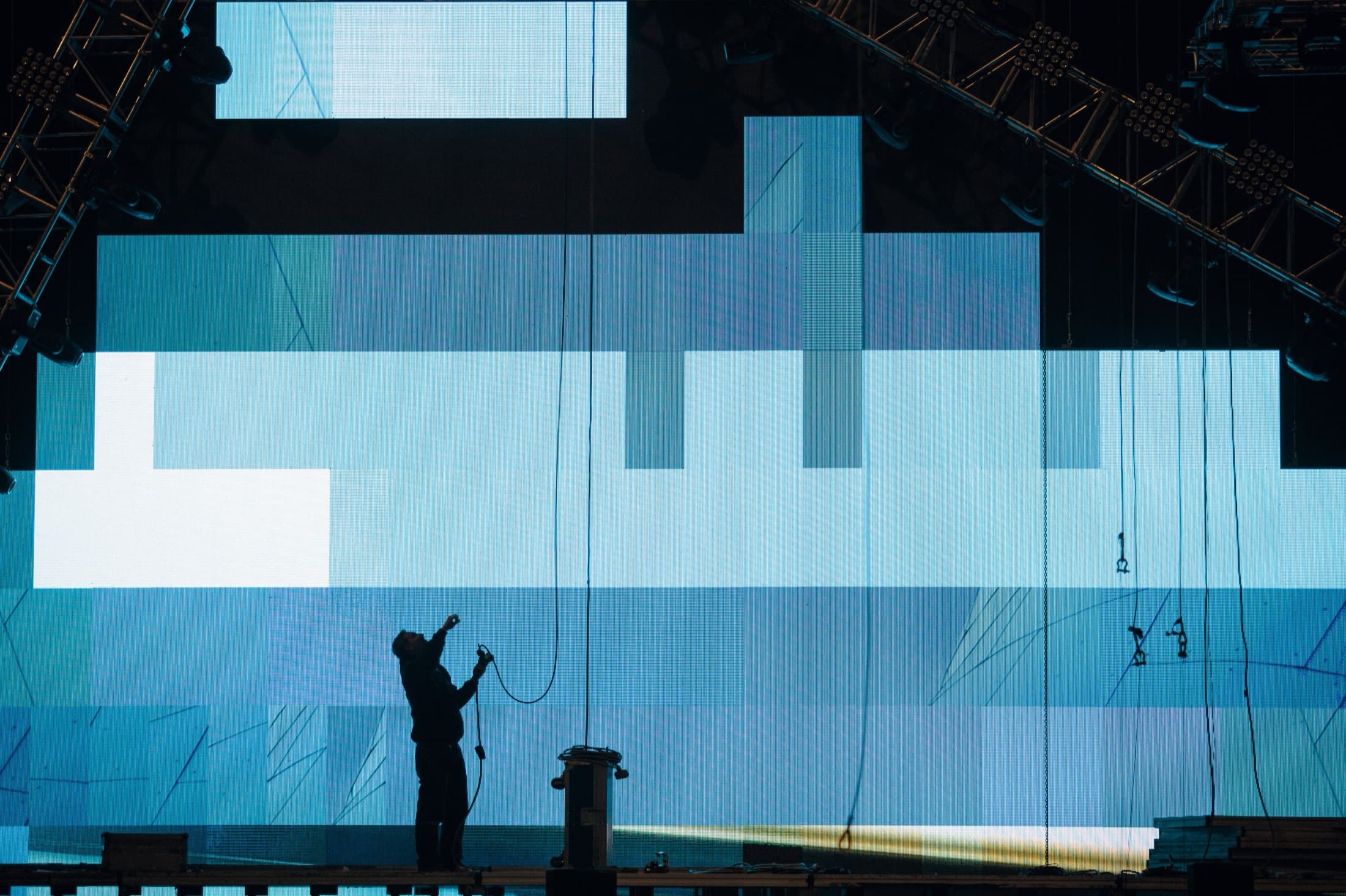 Technician in silhouette in front of a huge LED wall being installed on a stage